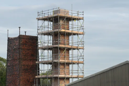 Pipe scaffolding built around a tall brick chimney beside another chimney